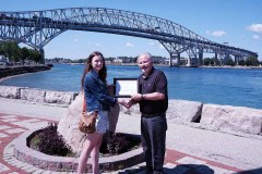 Heather Scott (left) is awarded with the Mary Jo Arnold Conservation Scholarship by St. Clair Region Conservation Authority Chair, Mike Stark (right) in front of the Bluewater Bridge in Sarnia.