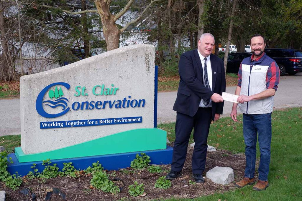 Two men standing beside a St. Clair Region Conservation Authority sign holding a cheque