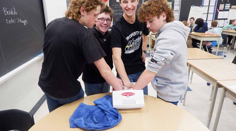 Four students standing with their hands in a cooler full of ice water.
